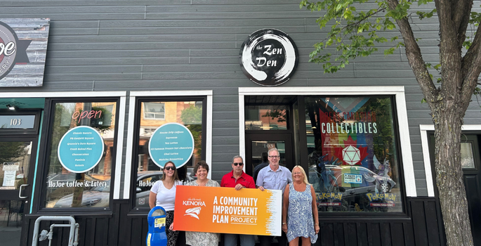 Group of people in front of a business holding a sign saying Community Improvement Plan Project